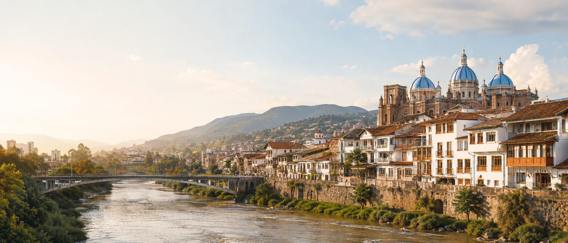 The Tomebamba river at golden hour, with the blue-tiled domes of the Catedral Nueva rising above the roofs of Cuenca.